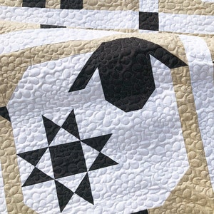 Puede incluir: Primer plano de un edred&oacute;n blanco y negro con un dise&ntilde;o de oveja. El edred&oacute;n presenta una gran cabeza de oveja negra y un patr&oacute;n de estrella en blanco y negro. El edred&oacute;n tiene un patr&oacute;n floral y detalles en beige y negro.