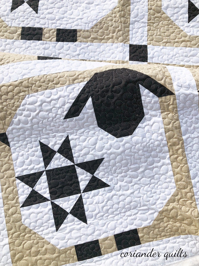Puede incluir: Primer plano de un edred&oacute;n blanco y negro con un dise&ntilde;o de oveja. El edred&oacute;n presenta una gran cabeza de oveja negra y un patr&oacute;n de estrella en blanco y negro. El edred&oacute;n tiene un patr&oacute;n floral y detalles en beige y negro.