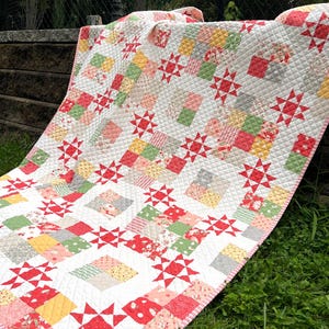 May include: A patchwork quilt featuring a repeating pattern of red eight-pointed stars interspersed with squares of various floral and geometric prints in shades of pink, yellow, green, and white, all finished with a diamond-shaped quilted texture.