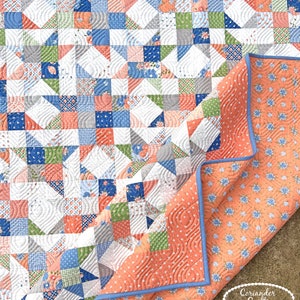 May include: A patchwork quilt in shades of blue, green, peach, grey, and white. The quilt has a floral pattern on the reverse and a light blue trim. The quilt is made of fabric. The quilt's dimensions are in centimeters.