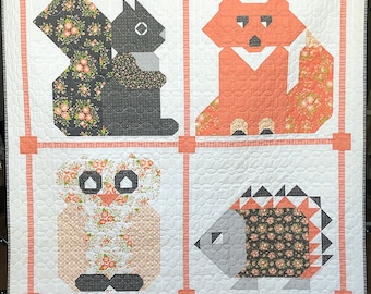 May include: A handmade quilt featuring four geometric animal designs: a squirrel, fox, owl, and hedgehog. Each animal is set within a square frame with a white background and coral accents. The animals are made of various patterned fabrics.