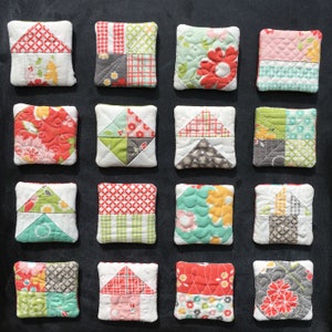 Könnte beinhalten: Eine Sammlung von sechzehn quadratischen Stoffuntersetzern mit verschiedenen Steppmustern. Jeder Untersetzer hat ein einzigartiges Design, darunter florale, geometrische und Patchwork-Motive in Rot-, Grün-, Gelb- und Grautönen. Die Untersetzer sind auf einer dunklen Oberfläche angeordnet.