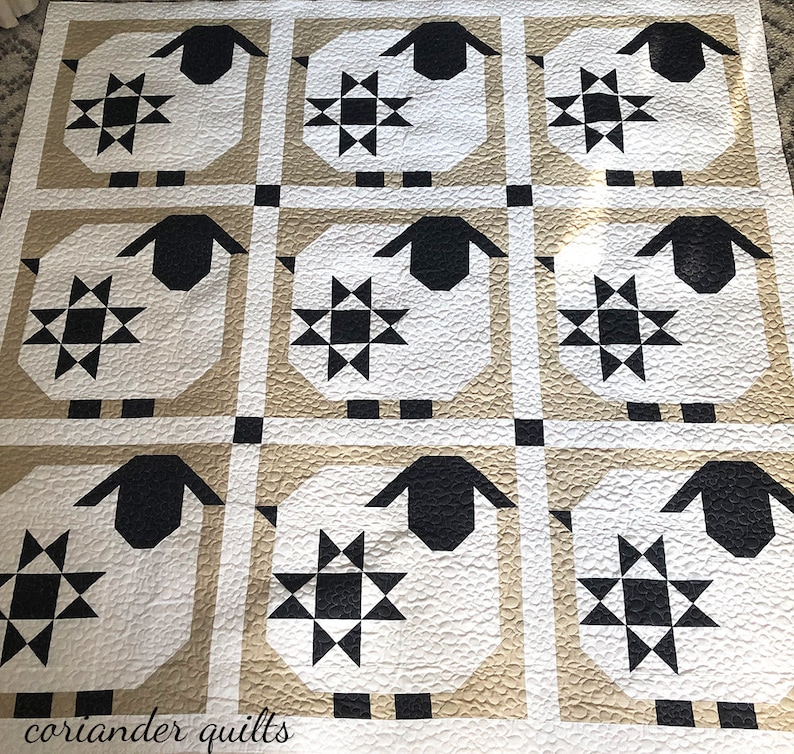 Puede incluir: Una colcha acolchada con un patr&oacute;n repetido de ovejas y estrellas. Las ovejas son blancas con caras y orejas negras, sobre una cuadr&iacute;cula beige y blanca. El texto "coriander quilts" es visible.
