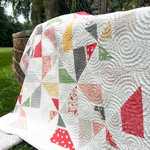 Peut inclure: Un quilt en patchwork avec un fond blanc et des motifs de matelassage en spirale complexes. Le design intègre diverses pièces de tissu triangulaires dans des tons de rouge, jaune, vert, gris et des imprimés floraux, disposés géométriquement.