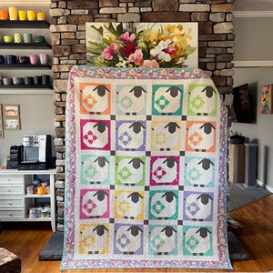 May include: A rectangular quilt featuring a grid of twenty blocks, each displaying a stylized sheep with a dark gray head and legs. The sheep are set against colorful square backgrounds in shades of orange, blue, green, pink, and yellow.