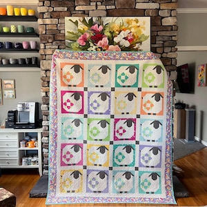 May include: A rectangular quilt featuring a grid of twenty blocks, each displaying a stylized sheep with a dark gray head and legs. The sheep are set against colorful square backgrounds in shades of orange, blue, green, pink, and yellow.
