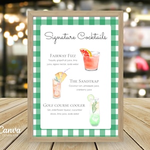 May include: A framed sign featuring the words "Signature Cocktails" and three cocktail illustrations. The sign has a green and white gingham border. The sign is displayed on a wooden table.