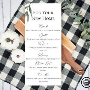 May include: A white rectangular sign with the text "For Your New Home" and blessings for bread, salt, wine, honey, olive oil, and a candle. The sign is on a wooden cutting board, with white pumpkins and a black and white checkered cloth.