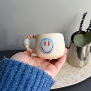 以下が含まれることがあります： 白のセラミックマグカップ、黒いハンドル、手書き風の「But First, Coffee」の文字。 マグカップは白い表面に置かれています。 マグカップの高さは約10cmです。