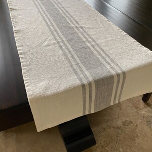 May include: A white table runner with gray stripes. The runner is laying on a dark wood table.