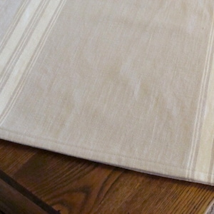 May include: A beige table runner with white stripes. The runner has a subtle linen texture and is hemmed on all sides.