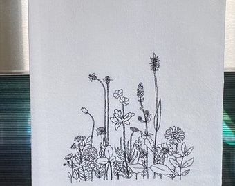 May include: A white kitchen towel with a black embroidered design of a field of wildflowers.