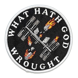 Può includere: Toppa ricamata con sfondo nero e bordo bianco. La toppa presenta un'immagine stilizzata di una stazione spaziale con fiamme e la scritta "WHAT HATH GOD WROUGHT" in lettere bianche.