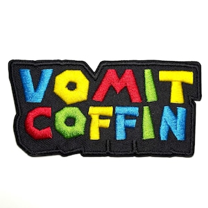 Puede incluir: Parche bordado con las palabras "VOMIT COFFIN" en letras coloridas estilo burbuja. Las letras son azules, amarillas, rojas, verdes y azules, sobre un fondo negro.