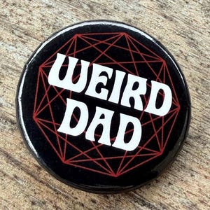 May include: Black button with a red geometric design and the text "WEIRD DAD" in white.