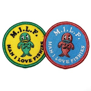 May include: Two round embroidered patches. One is yellow with a green border and a green fish-like creature. The other is blue with a red border and a red fish-like creature. Both have the text "M.I.L.F. MAN I LOVE FISHIES".