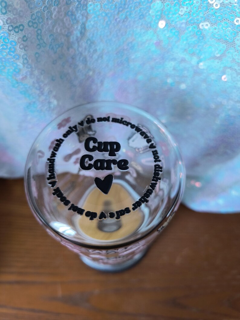 Op de afbeelding: Transparante glazen beker met de woorden "Cup Care" en een hartsymbool. De beker heeft tekst rond de rand met de tekst "handwash only", "do not soak", "do not microwave" en "dishwasher safe".