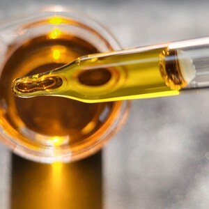 May include: A glass dropper with a clear glass tube and a yellow liquid inside. The dropper is over a glass beaker filled with a yellow liquid.