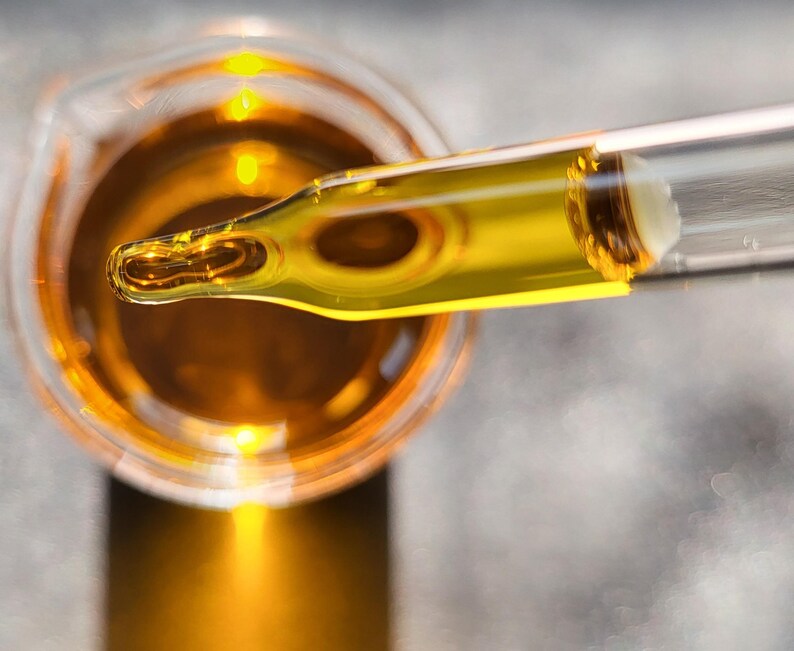 May include: A glass dropper with a clear glass tube and a yellow liquid inside. The dropper is over a glass beaker filled with a yellow liquid.