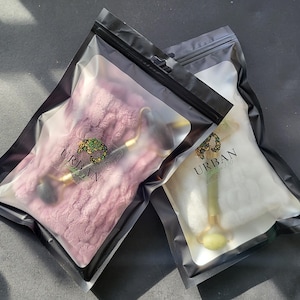 May include: Two sealed black and clear plastic bags, each containing a beauty product. One bag holds a pink item, the other a white item. Both bags have the word "URBAN" printed on them, along with a logo.