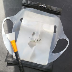 May include: A clear silicone face mask with a brush for applying skincare products. The mask has cutouts for the eyes, nose, and mouth. The packaging includes the text "URBAN Goddess 330".