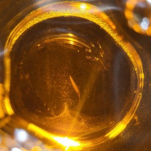 May include: Close-up of a clear glass jar filled with a golden liquid. The liquid is illuminated from below, creating a bright, shimmering effect.