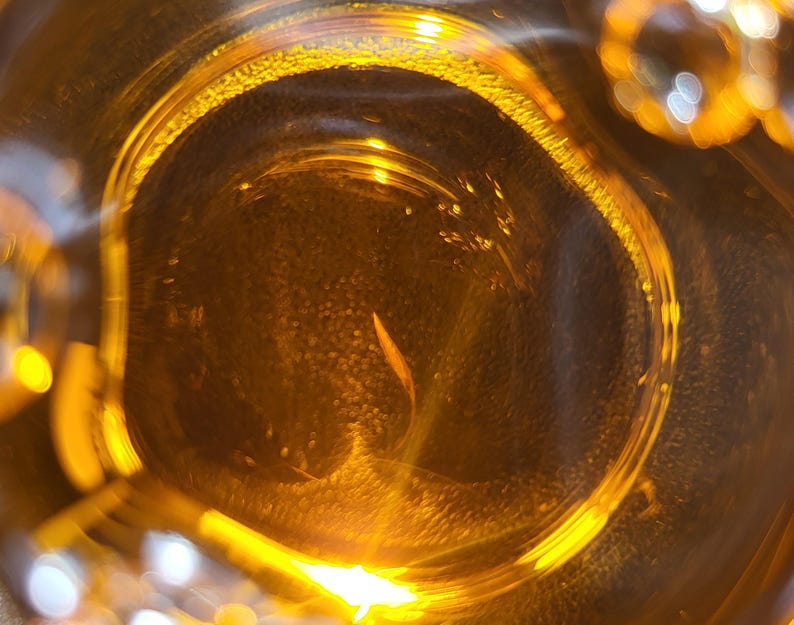 May include: Close-up of a clear glass jar filled with a golden liquid. The liquid is illuminated from below, creating a bright, shimmering effect.