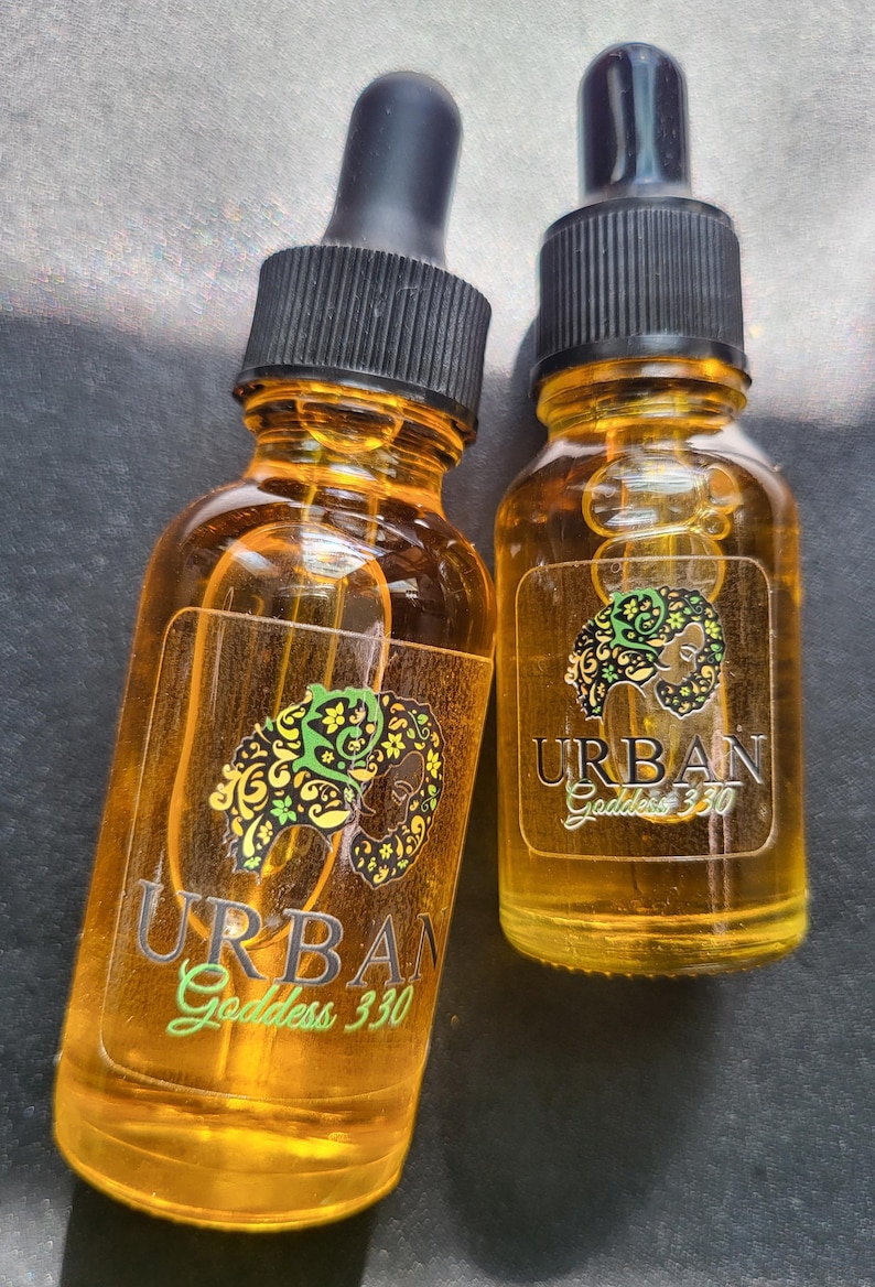 May include: Two amber glass bottles with dropper tops, both labeled "URBAN Goddess 330". The labels feature a stylized image of a woman's face with floral designs.