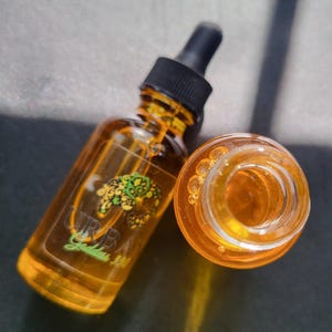 May include: A clear glass bottle with a dropper filled with a yellow liquid. The bottle has a black cap and a label that says "URBA Garden".
