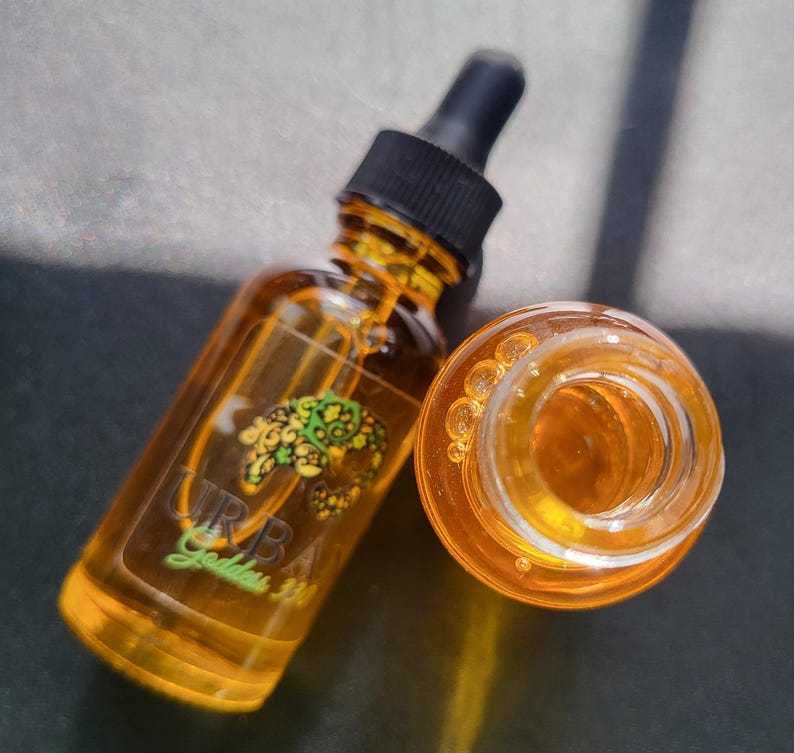 May include: A clear glass bottle with a dropper filled with a yellow liquid. The bottle has a black cap and a label that says "URBA Garden".