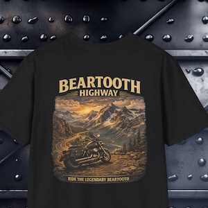 以下が含まれることがあります： 山道に駐車されたオートバイのグラフィックプリントが施された黒いTシャツ。上部にはBEARTOOTH HIGHWAY、下部にはRIDE THE LEGENDARY BEARTOOTHという文字が書かれています。曲がりくねった道、雪を頂いた山々、夕日の風景が描かれています。