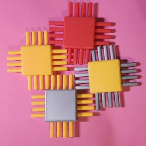 May include: Four colorful toy computer chips arranged on a pink background. The chips are red, yellow, and silver, with rectangular central components and radiating pins. The arrangement is symmetrical, creating a visually appealing pattern.
