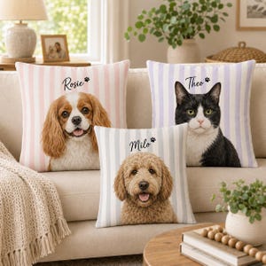 May include: Three square throw pillows with vertical stripes, each featuring a custom pet portrait and name. One pillow shows a Cavalier King Charles Spaniel named Rosie, one a black and white cat named Theo, and one a golden doodle named Milo.