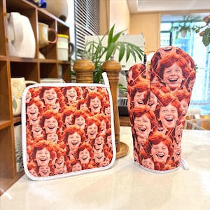 May include: A pot holder and oven mitt featuring a repeating pattern of a smiling person with red hair. The pot holder is square with a white border. The oven mitt is quilted and has a white loop for hanging.