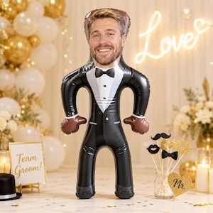 May include: A custom inflatable balloon shaped like a person wearing a black tuxedo with a white shirt and black bow tie. The balloon features a realistic printed photograph of a smiling man's face on the head area, creating a personalized party decoration.