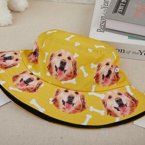 May include: Yellow bucket hat with a repeating pattern of golden retriever faces and white bone shapes. The hat has a black trim and a wide brim. The text "Person of the Year" is visible in the background.