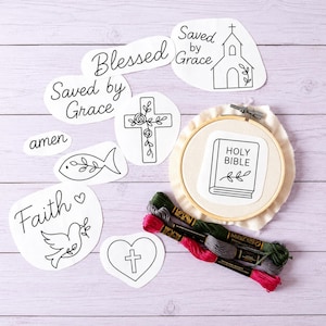 May include: A collection of white paper cutouts featuring black line art designs including a church, a cross with flowers, a fish, a dove, a heart with a cross, and the words Blessed, Saved by Grace, amen, and Faith, alongside an embroidery hoop.