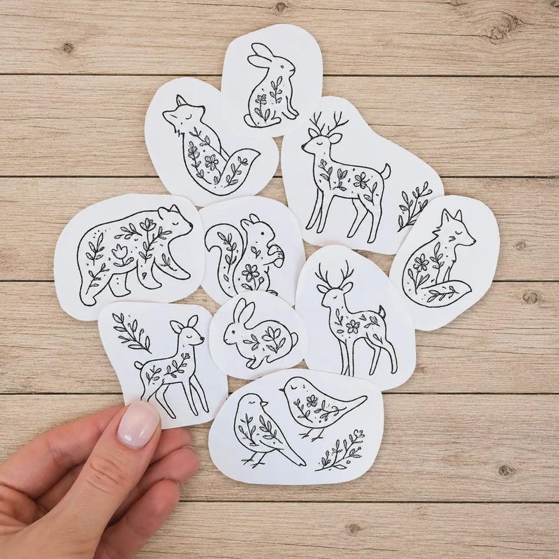 May include: A collection of white stickers featuring black line art illustrations of various forest animals including a bear, deer, fox, squirrel, rabbit, and birds, each decorated with delicate floral and botanical patterns on their bodies.