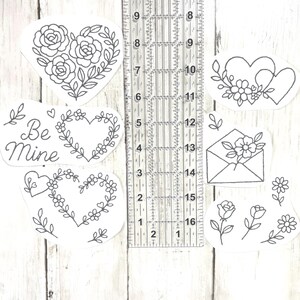 May include: A selection of black and white heart-shaped stickers featuring floral and leaf designs. One sticker has the text "Be Mine". A ruler is placed next to the stickers, showing measurements in centimetres.