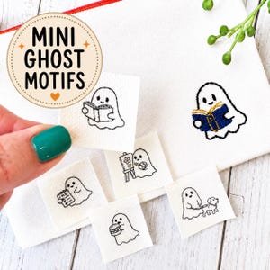 May include: A collection of small white fabric squares featuring black embroidered ghost motifs, including ghosts reading books, painting, eating a burger, and walking a dog. One ghost is held up, while others are arranged on a white canvas pouch.