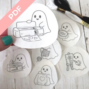 May include: A collection of white, circular embroidery patterns featuring cute ghost illustrations. Each ghost is engaged in a different activity, such as crafting, painting, and using a sewing machine. The word "PDF" is printed on a pink diagonal banner.