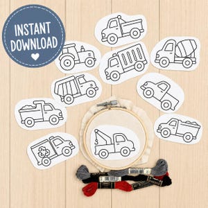 May include: A collection of black and white paper cutouts featuring various construction and utility vehicles, including a tractor, dump truck, and tow truck. A wooden embroidery hoop holds a tow truck cutout, accompanied by three skeins of embroidery floss.