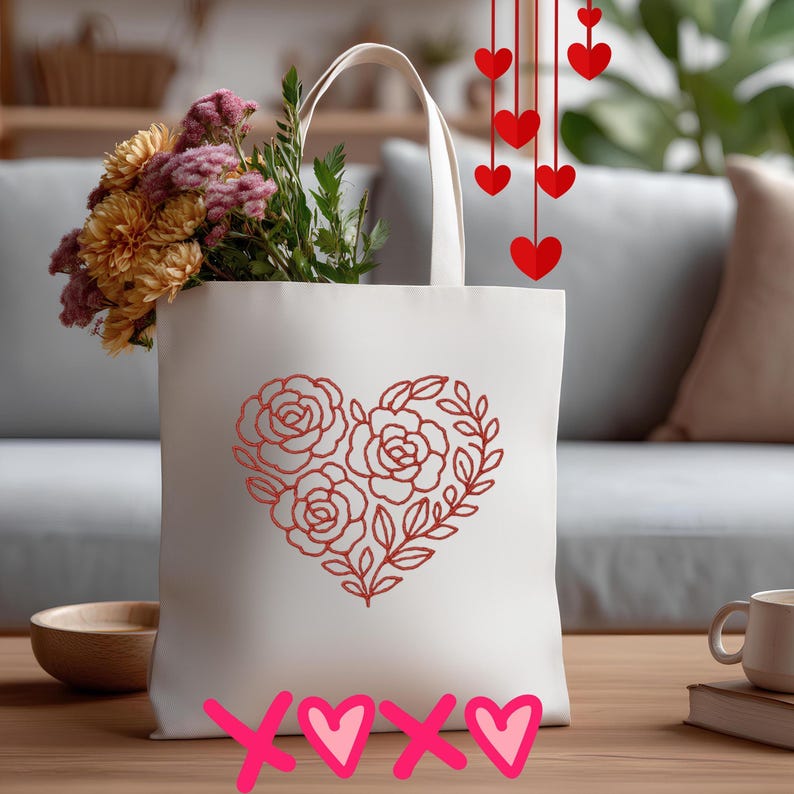 May include: A cream tote bag featuring a red rose heart design, filled with flowers. Red hearts hang from above. The words "xoxo" are written in pink at the bottom. A wooden bowl and a mug are on the table.
