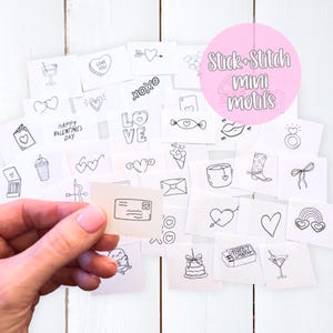May include: A collection of small, square, off-white paper motifs with black line drawings of hearts, arrows, and other Valentine's Day-themed images. The text "Stick+Stitch Mini motifs" is in a pink circle. A hand holds one motif.