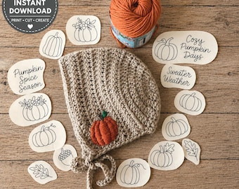 Könnte beinhalten: Eine beige gehäkelte Haube mit einer kleinen orangefarbenen Kürbisapplikation, einem Knäuel orangefarbenem Garn und mehreren weißen Papierausschnitten mit schwarzen Strichzeichnungen von Kürbissen, Blättern, Eicheln und Texten wie Pumpkin Spice Season.