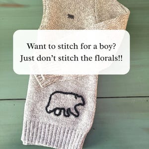 May include: A light beige knit fabric featuring a dark brown embroidered bear silhouette. The fabric displays the text: Want to stitch for a boy? Just don't stitch the florals!! The knit material has a ribbed texture at the bottom edge.