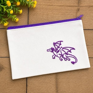 May include: A white rectangular canvas zipper pouch featuring a purple embroidered dragon design on the front. The pouch has a purple zipper closure along the top edge, providing a secure opening for storing small items inside the fabric container.