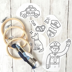May include: Embroidery kit featuring police-themed designs. Includes wooden hoops, embroidery floss in shades of blue and white, and printed patterns of a police car, badge, dog, and officer. Ideal for crafting and DIY projects.