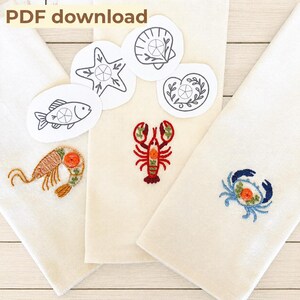 May include: Three off-white fabric towels featuring embroidered marine life designs including a tan shrimp, a red lobster, and a blue crab. Four white paper cutouts display black line art of a fish, starfish, seashell, and snail. Text reads PDF download.