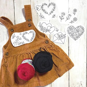 May include: A brown corduroy pinafore dress with a "Be Mine" patch and floral heart designs. Includes red and black yarn skeins, and several heart and floral embroidery patterns. The dress has button details.